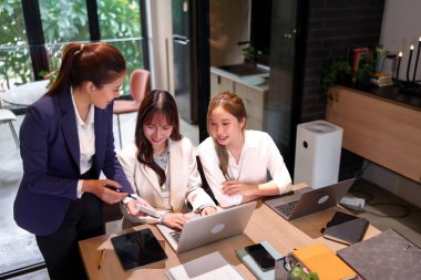 Üç genç Asyalı kadın bir ofis ortamında iş görüşlerini tartışmak için dizüstü bilgisayar kullanıyorlar. Takım çalışmasında başarı için proje planlaması ve beyin fırtınası yapıyorlar.