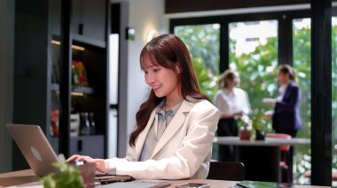 Genç bir Asyalı kadın iş görüşmesi sırasında dizüstü bilgisayarı üzerinde çalışıyor. Gülümsüyor ve ofiste mutlu görünüyor. O bilgisayarında yazarken iki kadın buluşuyor.