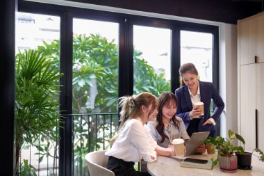 Bir grup Asyalı genç kadın modern ofis alanında proje ya da sunum için tablet kullanarak birlikte çalışıyorlar. Yeni iş fikrini tartışmak için ekip çalışması beyin fırtınası toplantısı..