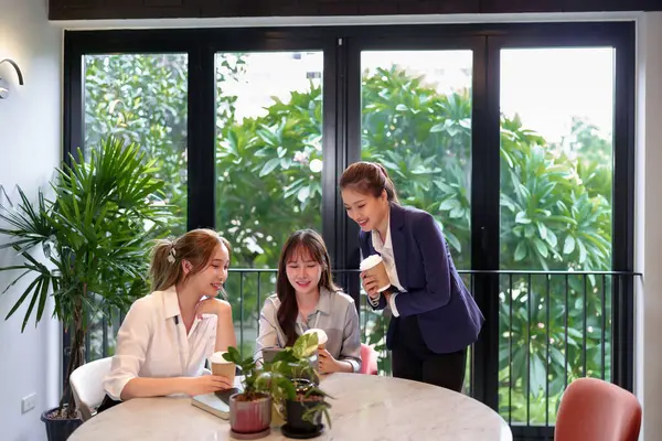Üç Asyalı kadın çalışma saatleri içinde modern bir toplantı yerinde kahve molası veriyorlar. İş dinamiklerini ve yeniliklerini göstermek için ideal bir tartışma ve işbirliği içerisindeler.