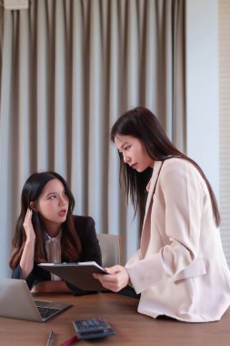 İki genç Asyalı kadın ofiste bir iş görüşmesi yapıyor. Belgeleri gözden geçiriyorlar ve strateji üzerinde işbirliği yapıyorlar. Profesyonel bir ortamda çalışıyorlar..