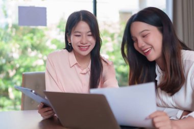 Bir iş planı üzerinde işbirliği yapan, belgeleri inceleyen, fikirleri paylaşan ve modern ofis ortamında verileri analiz eden iki genç Asyalı kadın. Takım çalışmasını göstermek için mükemmel..