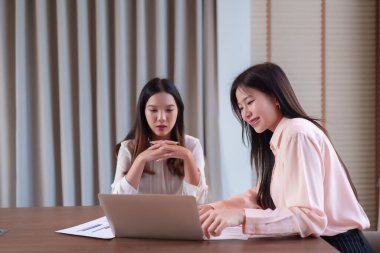 İki Asyalı kadın, yetişkin, modern bir ofiste bir iş projesinde işbirliği yapıyorlar. Stratejiyi tartışıyorlar, verileri analiz ediyorlar ve dizüstü bilgisayarda yazıyorlar. Resim takım çalışmasını yakalar.