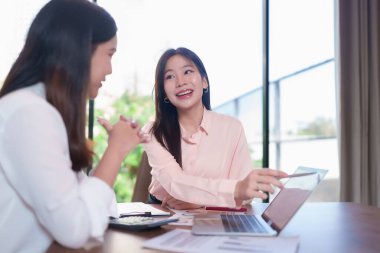 İki genç Asyalı kadın modern bir ofiste iş stratejisi üzerinde işbirliği yapıyorlar. Bir dizüstü bilgisayardaki verileri analiz ediyorlar, başlangıç başarısı için beyin fırtınası yapıyorlar. Sahne takım çalışmasını yakalar.