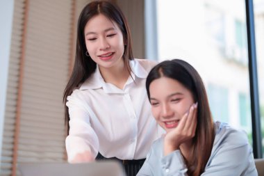 İki genç Asyalı kadın, profesyonel bir ofis ortamında bir proje üzerinde birlikte çalışıyorlar. Takım çalışmasını ve işbirliğini gösteren bir dizüstü bilgisayara odaklandılar. Bu görüntü iş, takım çalışması ve teknoloji için kullanılabilir