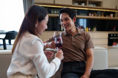 Aşkın ve kutlamanın özünü kırmızı şarapla kadeh kaldıran Asyalı bir çiftin görüntüsüyle paylaşın neşeli anları paylaşın bir ev buluşmasının romantizminin tadını çıkarın