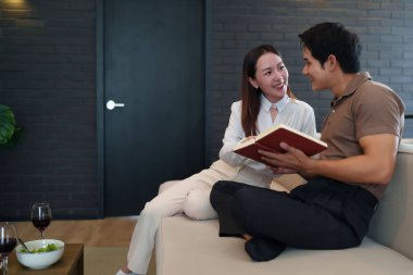 Yetişkin bir Asyalı çift evde kanepede oturup kitap okuyor. Oturma odasındaki masada şarap ve salatayla rahatça vakit geçiriyorlar..