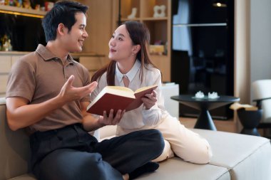 Sevgi dolu bir Asyalı çift birlikte kitap okuyarak sakin bir anın tadını çıkarıyor. Kanepelerinde rahat bir şekilde otururlar. Modern yaşam alanlarında mutlu ve mutlu görünürler.