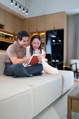 Genç bir Asyalı çift evde rahat bir kanepede rahatlıyor ve kitap okuyor. Kadın ve erkek oturma odasında kitap okuyarak eğleniyor gibi görünüyorlar..