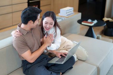 Asyalı gülümseyen bir çift oturma odasında dizüstü bilgisayar kullanıyor Asyalı bir adam ve kadın bilgisayar planlamada birlikte çalışıyorlar Mutlu partnerler evde kanepede birlikte dinleniyorlar