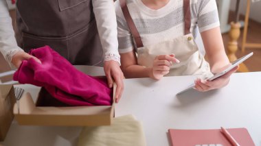 İki Asyalı kadın ellerinde tabletle teslimat için çevrimiçi siparişler paketliyor. Ev sahibi bir butik mağazasında perakende satış mağazası ve pazar yeri için küçük işletme fikirleri..