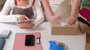 Asyalı yetişkin kadınlar siparişleri kontrol etmek, stokları kontrol etmek ve müşterilere teslimat için kutuları hazırlamak için tablet kullanıyorlar. Küçük işletme sahipleri çevrimiçi bir mağazada çalışıyor..