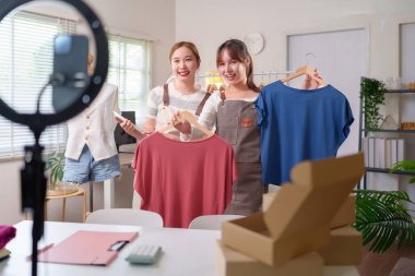 İki genç Asyalı kadın, sosyal medyadaki işleri için moda kıyafetlerini canlı olarak yayınlıyor, müşterilerle bağlantı kurmayı, satışları artırmayı ve marka tanımayı artırmayı hedefliyorlar..