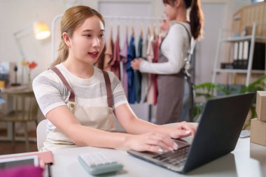 Asyalı bir kadın çevrimiçi giyim mağazasını yönetmek için dizüstü bilgisayar kullanıyor. Envanter yönetimine ve iş büyümesini ve satışları artırmak için müşteri hizmetleri sunmaya odaklanıyor..