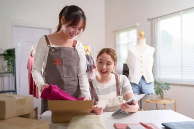 İki genç Asyalı kadın evlerinde online bir giyim mağazası işletiyorlar. Müşteri siparişlerini kontrol ediyorlar ve nakliye için eşya paketliyorlar. Onlar mutlu ve başarılı küçük işletme sahipleri..