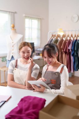 İki genç Asyalı kadın online giyim mağazaları için bir tablet kullanarak iş birliği yapıyorlar. Moda girişimlerinde insan cep telefonu, iş ve müşteri ilişkilerini geliştirmek yoluyla iletişim kurar.