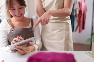 Bu resimde, tablet kullanarak gülümseyen Asyalı genç kadınlar ve onun asistanı ellerini gösteriyor, evde online iş ya da dış ticaret için birlikte çalışıyorlar.