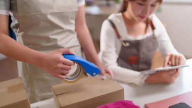 Kargo için karton kutulara eşya koyan Asyalı kadınları kapatın. Ofislerinden online iş siparişlerini yönetmek için bant kesicisi ve tablet cihazı kullanıyorlar..