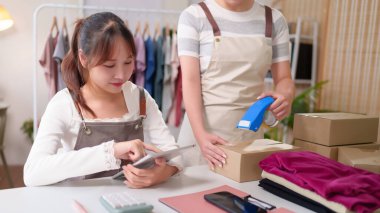 Çevrimiçi iş yürüten Asyalı genç kadınlar sipariş paketlerini karton kutulara koyup teslim etmek için tablet üzerindeki bant kontrol adresi bilgilerini kullanıyorlar..