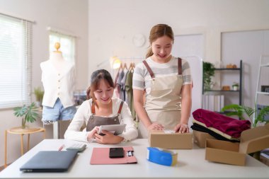 Çevrimiçi moda mağazalarında çalışan iki genç Asyalı kadın. Biri nakliye için sipariş hazırlamak. Diğeri ise envanter yönetimi ve müşteri hizmetleri için bir tablet kullanıyor..