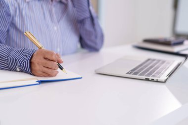 Dizüstü bilgisayarın yanındaki beyaz masaya kalem yazısıyla yaşlı Asyalı kadının eline odaklan. İşletme eğitimi ya da fikir üretmek için harika çekimler..