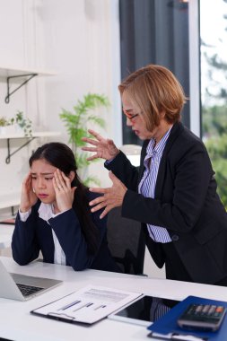 Asyalı bir kadın tarafından resmedilen ve yaşlı bir meslektaşından baskı gören iş stresini keşfedin. Görüntü takım sorunlarını ve yönetim biçimi etkisini gösterir.