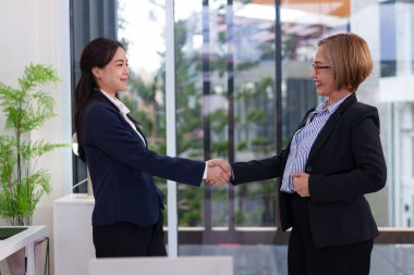 Asyalı kadınların el sıkışması. Bir kadın genç, diğeri yaşlı. Birlikte çalışarak ortaklık yapıyorlar. Mutlu çalışma anları, dost takım.