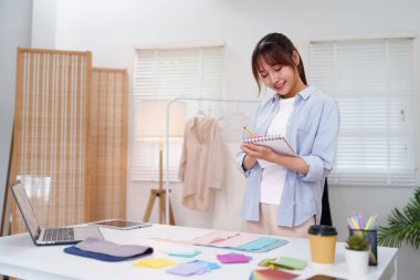 Asyalı genç bir kadın moda tasarımcısı stüdyosunda yaratıcı terzilik işi için kumaş örnekleri seçiyor.