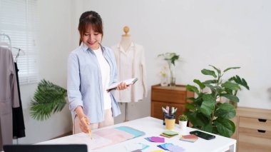 Asyalı genç girişimci kadın stüdyosunda yeni kıyafet tasarımları çiziyor. Küçük bir işletme sahibi ve yaratıcı terzilik projesi üzerinde çalışıyor..