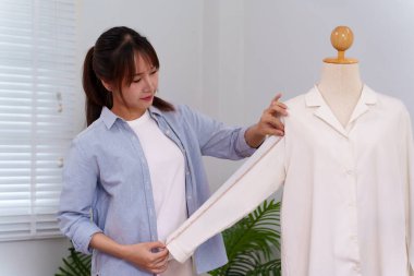 Genç bir Asyalı kadın terzi mankenin kol uzunluğunu ölçmek için mezura kullanıyor. Moda kıyafetleri ve terzilik tasarlıyor..