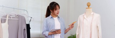 Genç bir Asyalı kadın bir mankenin yanında kıyafet tasarlıyor. Giysilerin uyduğundan emin olmak için bir mezura kullanıyor. Moda veya tasarım içeriği için mükemmel