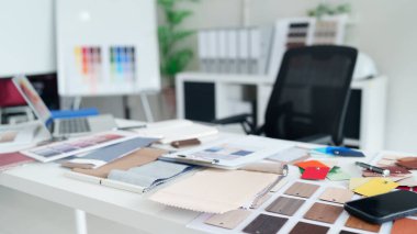 Bir tasarımcının masasında modern ofiste yaratıcı proje planlaması ve yönetimini geliştirmek için kullanılan çeşitli renk paletleri kumaşı ve malzeme örnekleri sergilenmektedir.