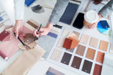 Asyalı bir yetişkin iç mimar özenle kumaş örnekleri ve malzeme örnekleri seçiyor. Yeni bir ev dekorasyonu projesi için renk paletini seçiyorlar.