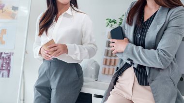 İki yetişkin Asyalı kadın modern bir stüdyoda dekorasyon malzemesi seçmek için iç tasarım projeleri planlıyorlar. Ofis alanını tartışan mimarlar..