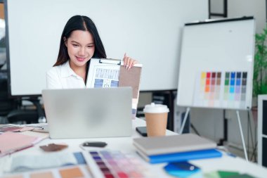 Asyalı genç bir kadın çevrimiçi toplantı yoluyla iç tasarım projesini malzeme palet örnekleriyle sunuyor. İç tasarım fikirleri ve yenileme kavramları ilham verici..