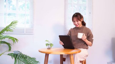 Bu resim, evde dijital tablet kullanırken gülümseyen Asyalı genç bir kadını sabah içeceğinin keyfini çıkarırken gösteriyor. Modern günlük rutinlerin özünü yakalıyor. Gelişmiş teknolojinin kişisel yaşamla sorunsuz bir şekilde bütünleşmesini sağlıyor. Onun...