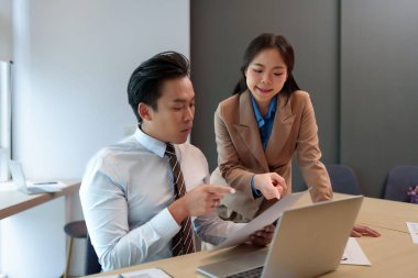 Ofis toplantısında işbirliği yapan iki Asyalı yetişkin profesyonel pazar veri analizini tartışıyor iş stratejisini gözden geçiriyorlar gelecekteki büyüme verimliliğini planlıyorlar