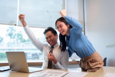 İki Asyalı profesyonel yetişkin heyecanlı bir mutluluk ifadesi sergiliyor. Başarılı bir anı başarıyla tamamlayıp ofis ortamındaki veri analizlerini gözden geçiriyorlar.