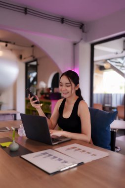 Mutlu Asyalı kadın göçebe modern çalışma alanında bilgisayarla çalışıyor. Uzaktan çalışan, esnek çalışma ortamının keyfini çıkarıyor.