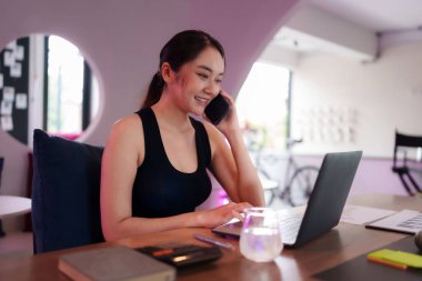 Yetişkin Asyalı kadın, uzak profesyoneller için mükemmel, modern esnek bir çalışma alanında telefon iletişimini ve dizüstü bilgisayarları verimli bir şekilde yönetir..