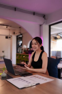 Gülümseyen Asyalı kadın dinamik bir ortak çalışma merkezinden projelerde işbirliği yapıyor. O, esnek bir iş yaşam tarzını benimseme görevlerini yönetir..