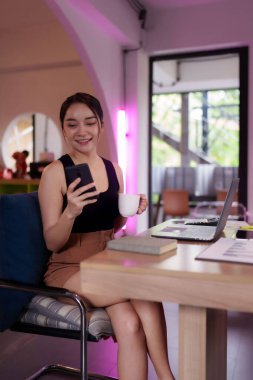 Neşeli Asyalı kadın kahve ve cep telefonuyla kısa bir mola veriyor. Bir kadın girişimci, ortak çalışma alanlarında ilham bulur.