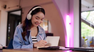 Mutlu, genç, profesyonel bir kadın işinden zevk alır. Gülümseyen kız öğrenci, modern bir masadaki deftere yazarken ses dinler.