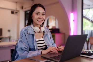 Asyalı serbest çalışan kadın gülümseme, canlı bir iş merkezinde bilgisayarla uzaktan çalışmaktan hoşlanıyor. Modern ofis ortamında üretken dijital göçebe yaşam tarzı.