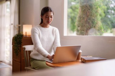 Asyalı kadın evde uzaktan bilgisayarla çalışıyor. Verimlilik gevşemesi ve çevrimiçi çalışma için ideal iç mekan ayarları.