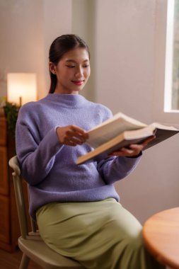 Asyalı kadın sıcak ev atmosferinde kitap okumayı sever. Sakin ve huzurlu bir şekilde sakin bir aktiviteye katılıyor..