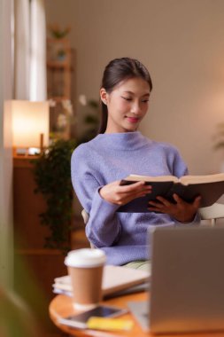 Kitaplara dalmış genç Asyalı kadın ev ortamında bilgi topluyor boş zamanlarında kişisel gelişim sessizce düşünüyor.