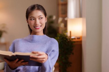 Evde kitap okuyan rahat Asyalı kadın rahatlık bilgisi ve rahatlık sağlıyor. Kapalı alanda barışçıl aktivitelerden hoşlanır..