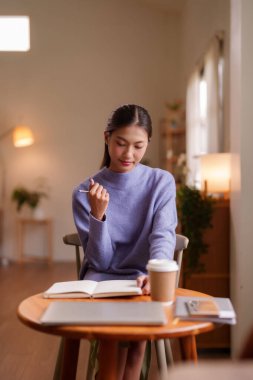 Asyalı kadın özenle ev masasına notlar yazıyor. Huzurlu bir ortam. Günlük görevlerine yoğunlaşarak sakin ve üretken anlardan hoşlanıyor.