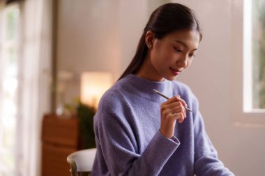 Genç Asyalı kadın düşünceli bir şekilde evde çalışıyor. Huzurlu bir ortamda çalışmaya ya da mesleki görevlere adanmışlığı yakalamak.